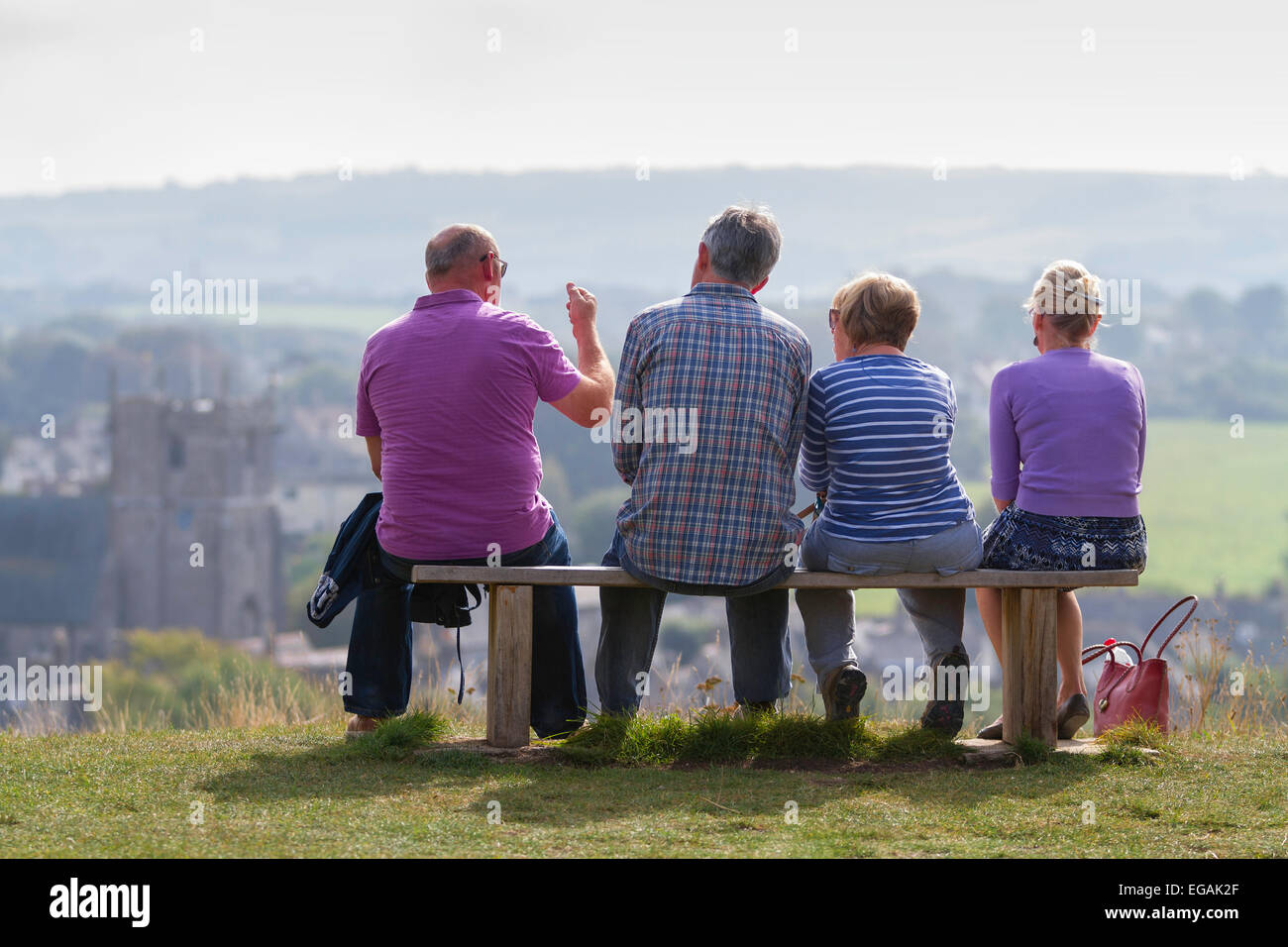 Vier aktive Senioren sitzt auf einer Holzbank, gesehen von hinten, mit Blick auf die Stadt Corfe in Dorset. Stockfoto