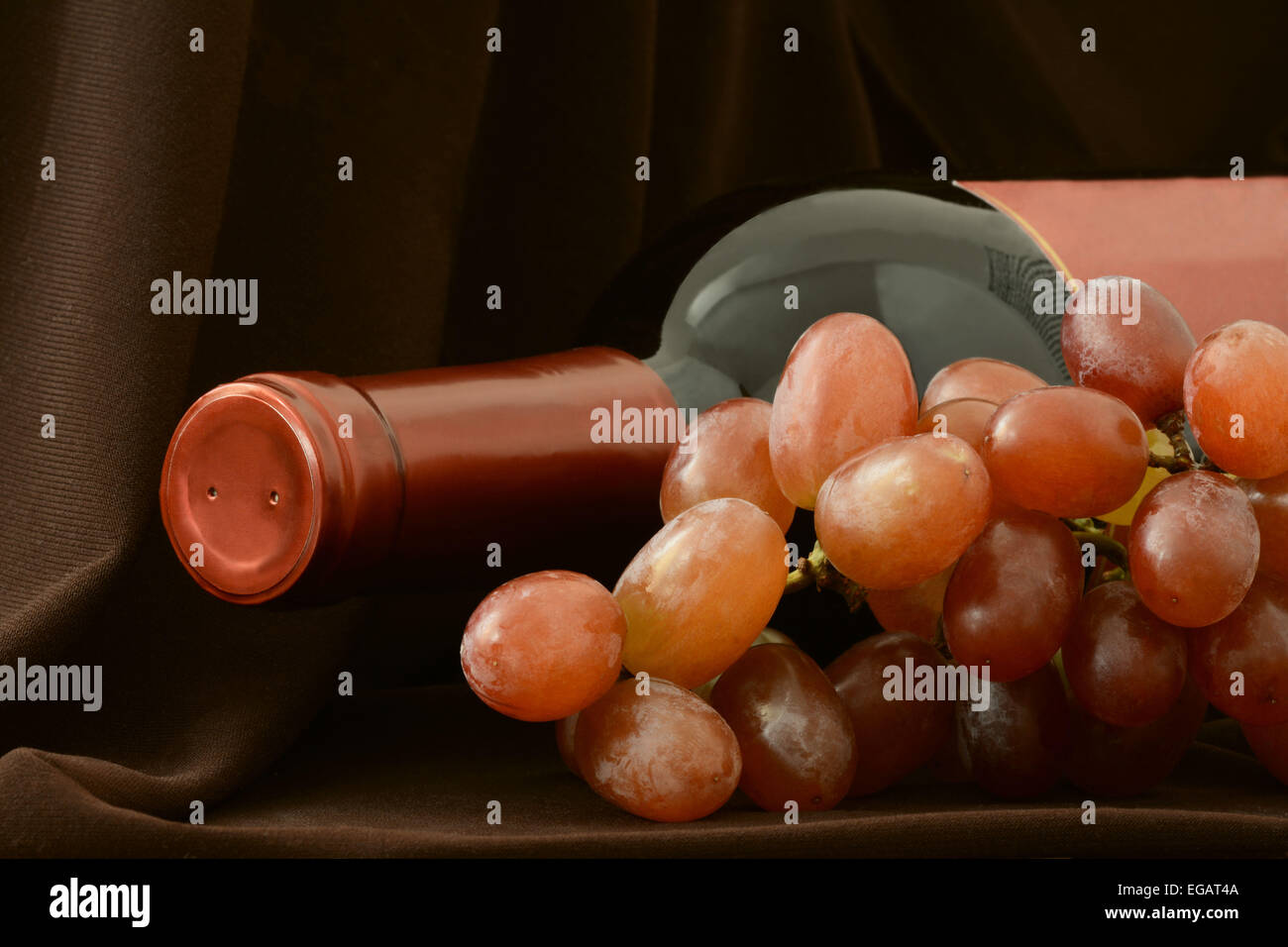Flasche Rotwein und Weintraube auf einem dunklen braunen Hintergrund liegend Stockfoto