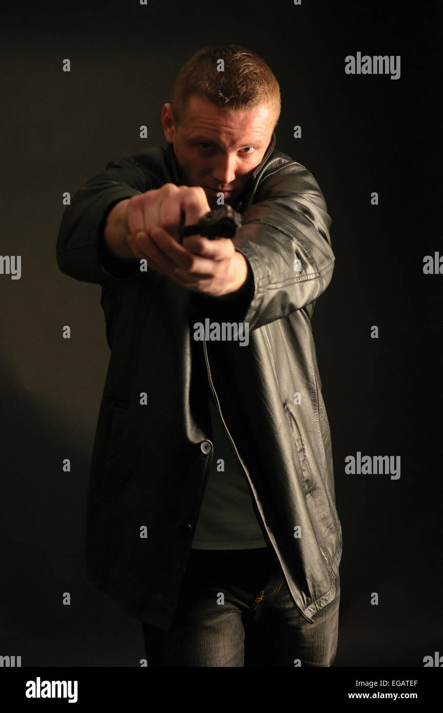 Ein Mann (Modell) trägt eine Lederjacke weist eine Handfeuerwaffe Stockfoto