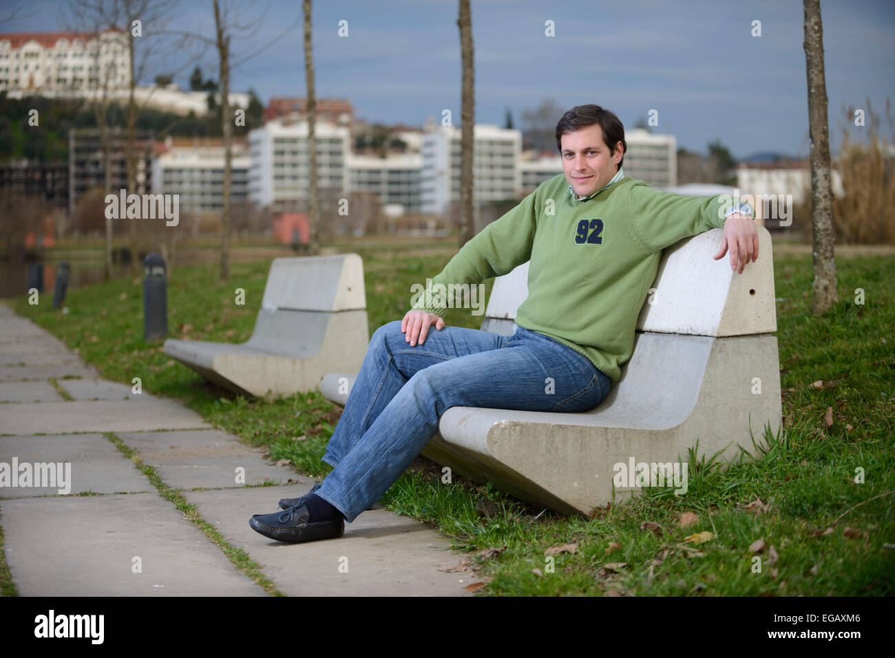 Junger Mann sitzt auf einer Zement-Bank in einem park Stockfoto