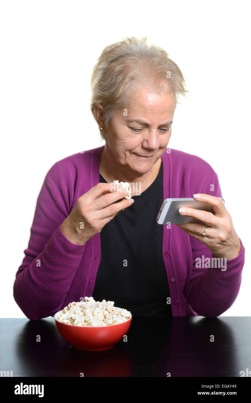 Mittlere gealterte Frau Essen Popcorn beim Ansehen eines Films auf einem Apple iPhone Smartphone Stockfoto