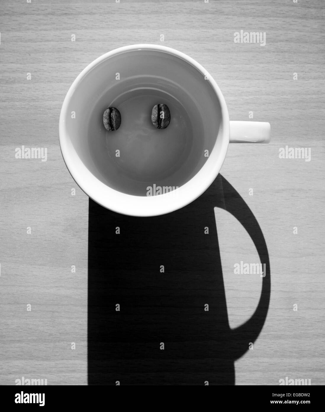 Abstrakte Kaffee Konzept, weiße leere Tasse mit Bohnen und Schatten sieht aus wie ein lustiger Mann Zeichen auf Holztisch Stockfoto
