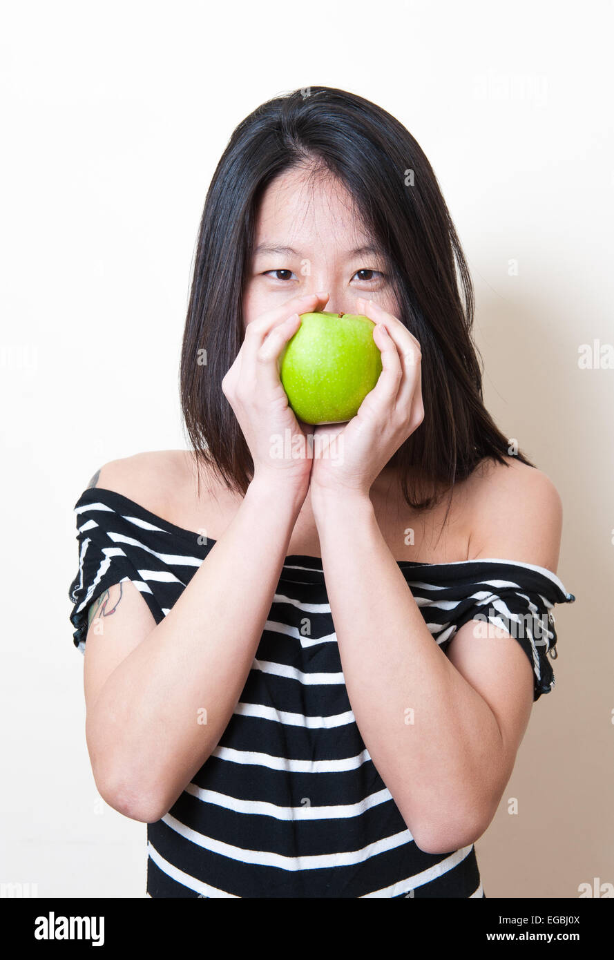 Junge schöne asiatische Frau Porträt Lächeln mit grünem Apfel über Mund auf weißem Hintergrund Stockfoto