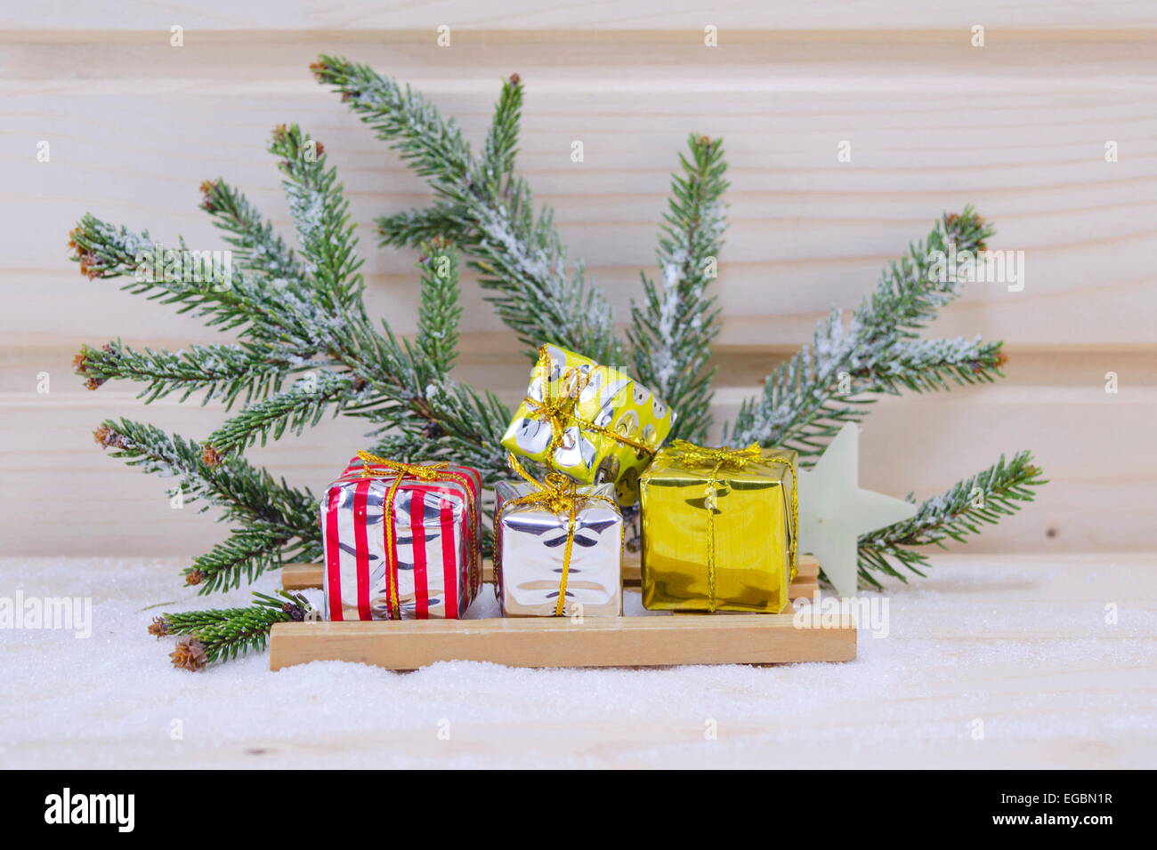 Weihnachtsgeschenke auf einem Schlitten mit einer Tanne-Niederlassung im Hintergrund auf einer Holzfläche mit Schnee bedeckt Stockfoto