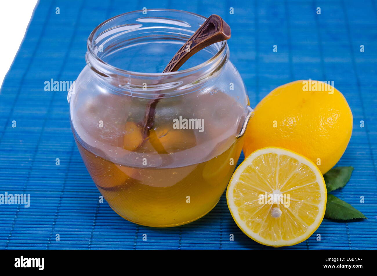 Ein Glas halb mit Honig und Zitronen auf blauem Hintergrund mit einem Vintage Holzlöffel voll Stockfoto