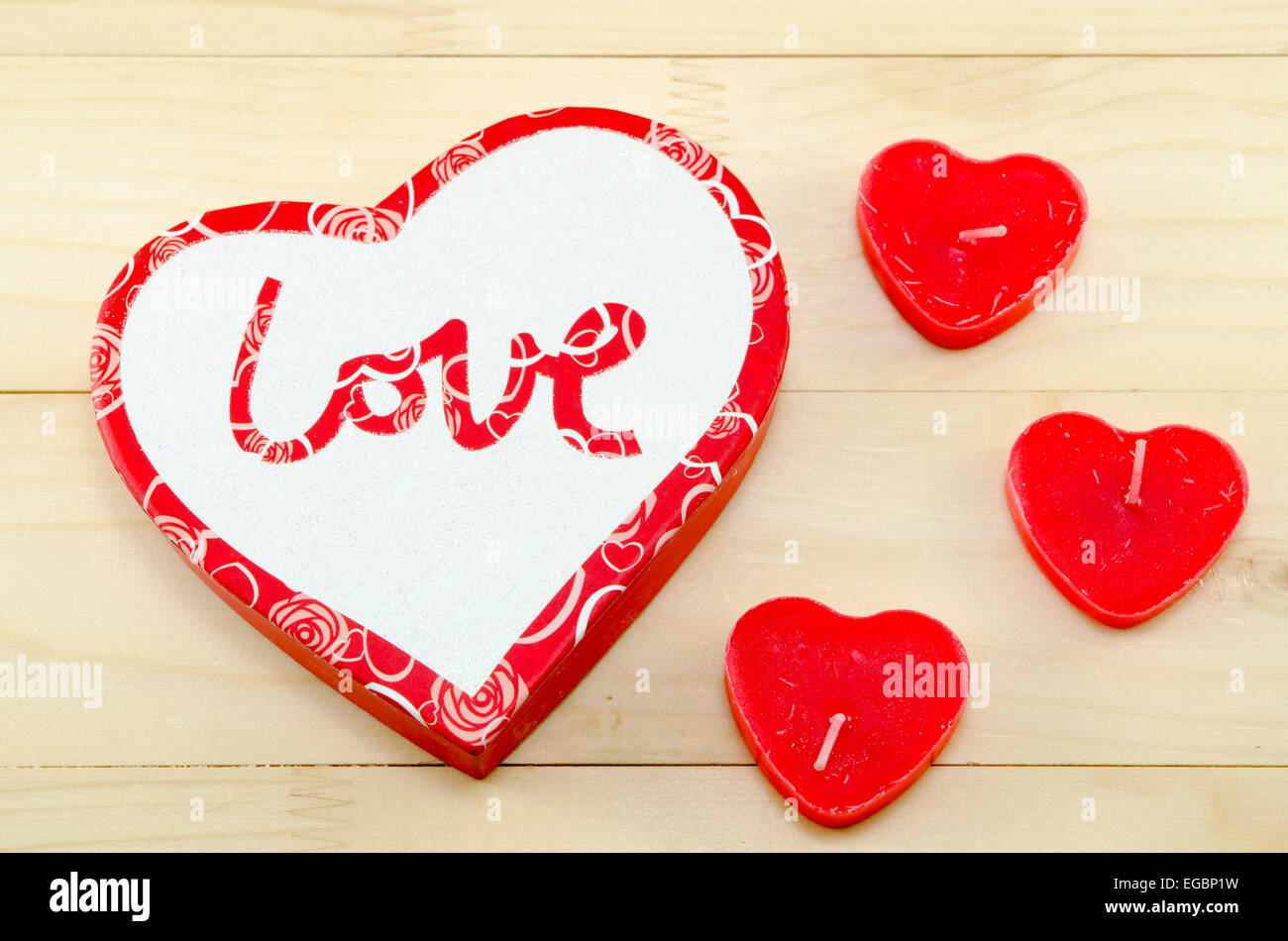 Herzförmige rote Kerzen und eine Schachtel mit dem Wort "Liebe" geschrieben, auf einem hölzernen Hintergrund Stockfoto