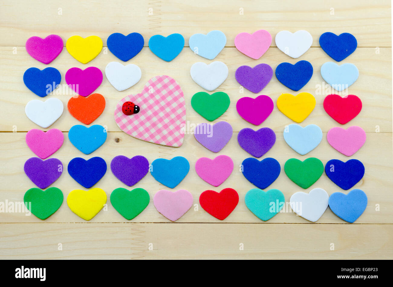 Viele bunte Herzen auf einem Schreibtisch mit großem Karo Herz in der Mitte verziert mit einem Marienkäfer Stockfoto