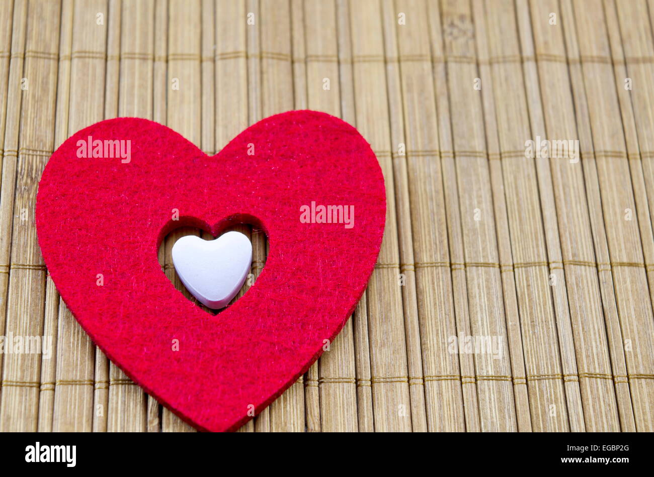 Großes rotes Herz mit einem kleineren weißen Herz im Inneren auf einer Bambus-Tischdecke Stockfoto