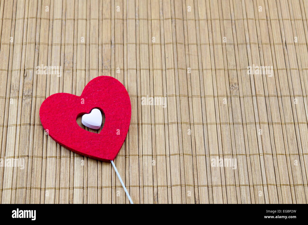 Großes rotes Herz mit einem kleineren weißen Herz im Inneren auf einer Bambus-Tischdecke Stockfoto