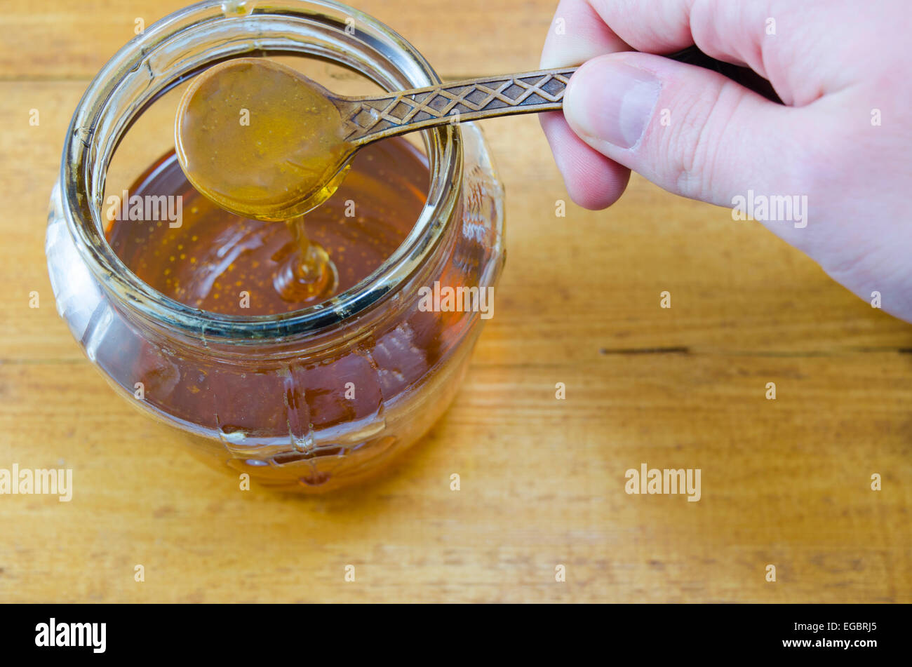 Hand mit einem hölzernen Löffel Honig tropft in das Glas Stockfoto