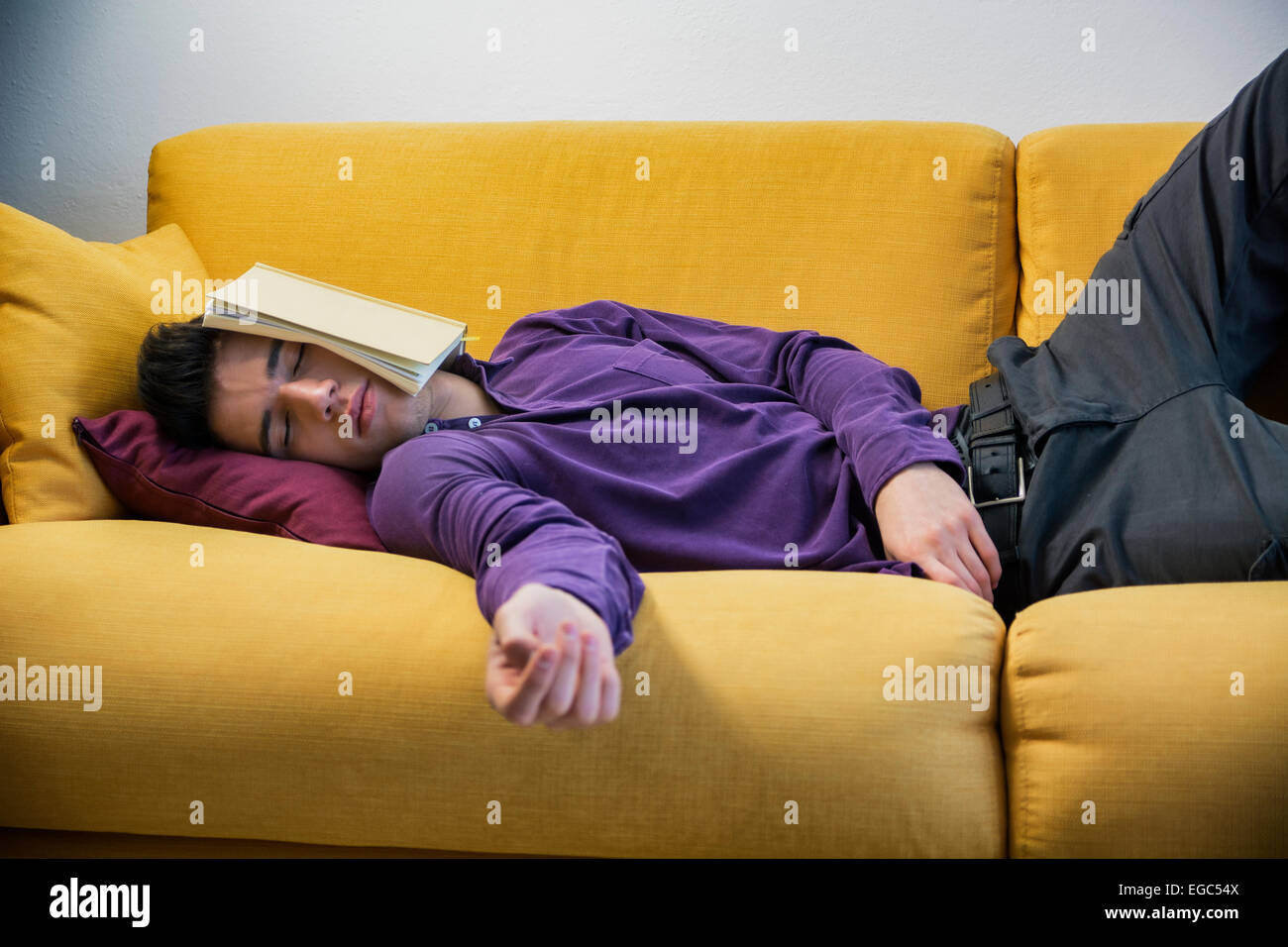 Über-arbeitete, müder junger Mann zu Hause schlafen unter Buch Stockfoto