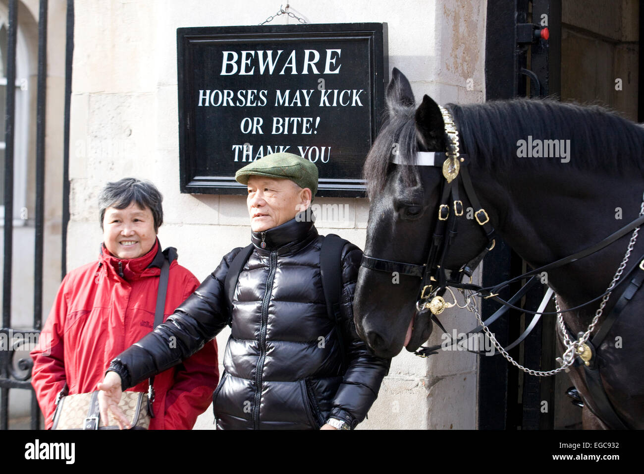 Asiatische Touristen am Horseguards Parade stehen unter ein Schild mit der Aufschrift "Achtung Pferde können kick oder beißen Danke" mit dem Pferd zu versuchen, zu ersticken Stockfoto