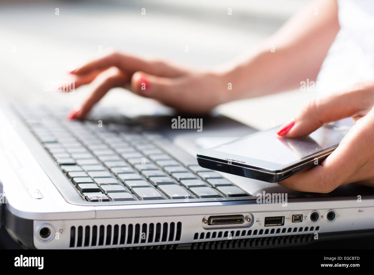 Hände eine Geschäftsfrau auf einer Computertastatur tippen und Telefon in der anderen Hand hält Stockfoto