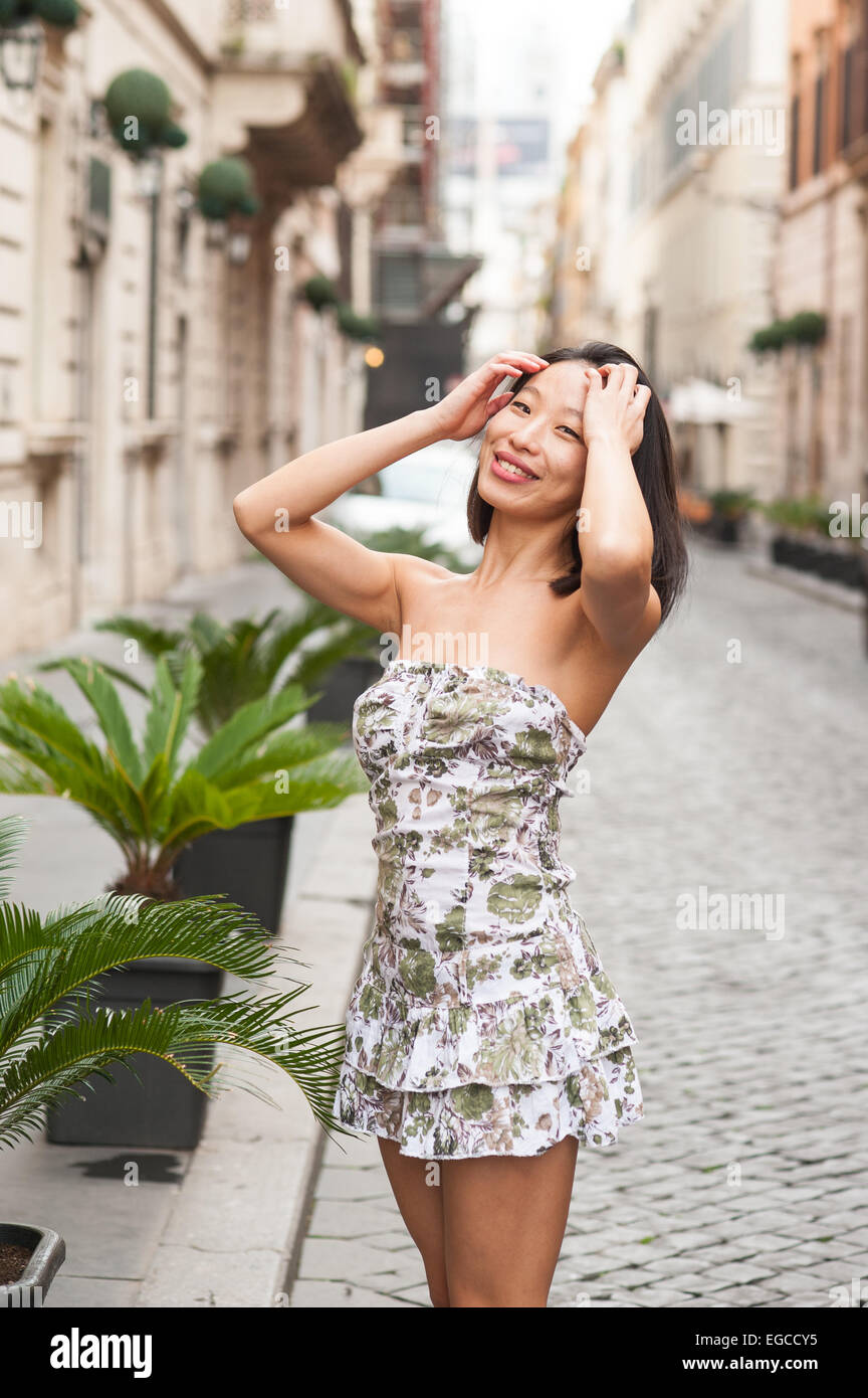 Mode sexy Asiatin entspannt posiert auf europäischen Straße Hände auf Haar, sonnigen Tag Stockfoto