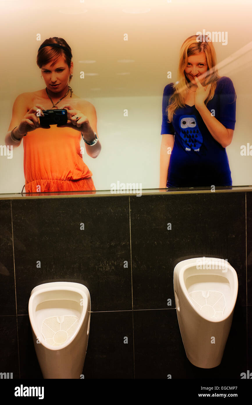 Bilder von jungen Frauen über Urinale in einer Herrentoilette angeordnet, um über Männlichkeit Männer lustig zu machen. Stockfoto
