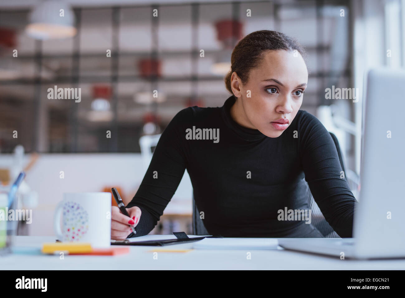 Bild der jungen Unternehmerin Blick auf Laptop während der Arbeit an ihrem Schreibtisch. Weibliche Webdesigner Notizen aus dem Internet. Stockfoto