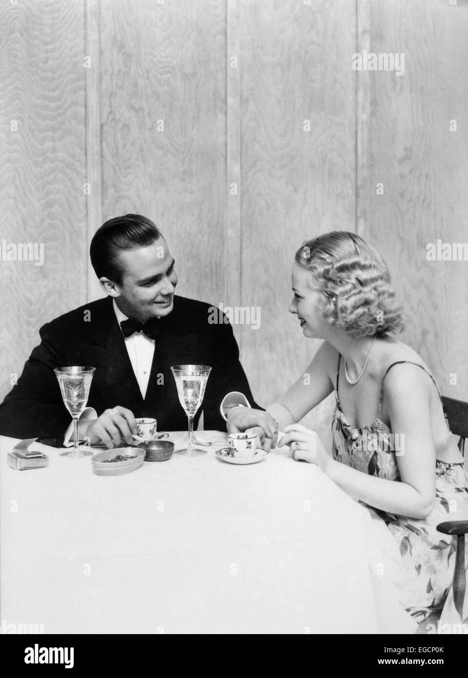 1930ER JAHREN PAAR MANN FRAU FORMELLE KLEIDUNG SMOKING SITZEN TABELLE ROMANTISCHES DINNER ROMANCE CRYSTAL KELCHE DATUM Stockfoto