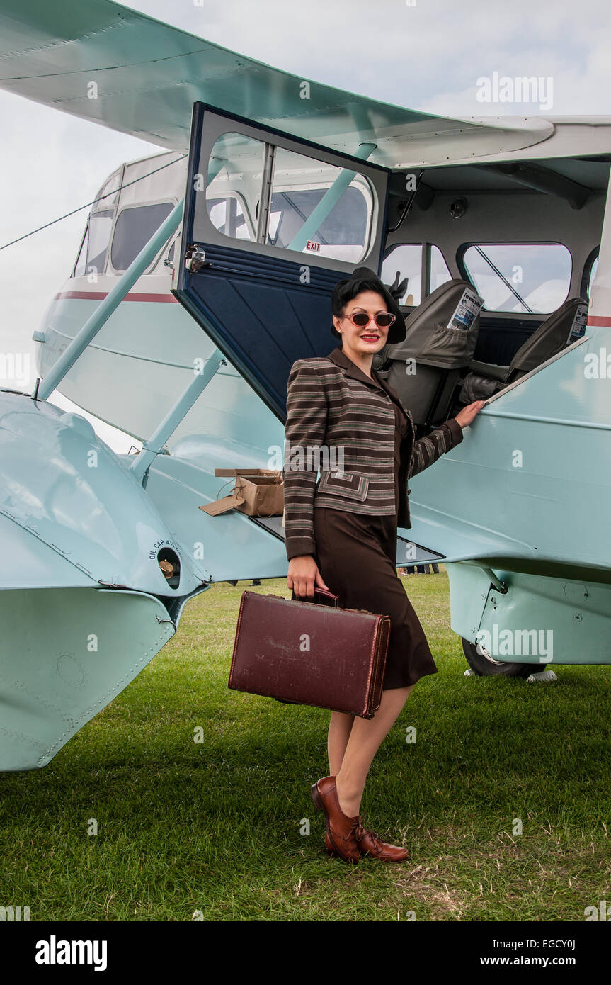 Ein Mädchen in Kostümen neben einem Flugzeug am Goodwood Revival 2014 posieren. Frauen in klassischen Vintage Zeitraum Kleid in der Luftfahrt. Mode Stockfoto