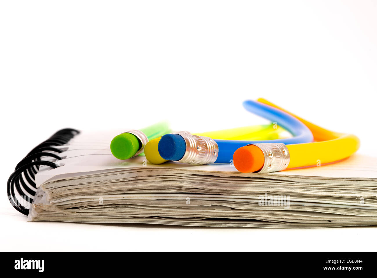 Vier bunte Bleistifte, die biegen alle seltsam, liegend auf einem Notebook. Stockfoto