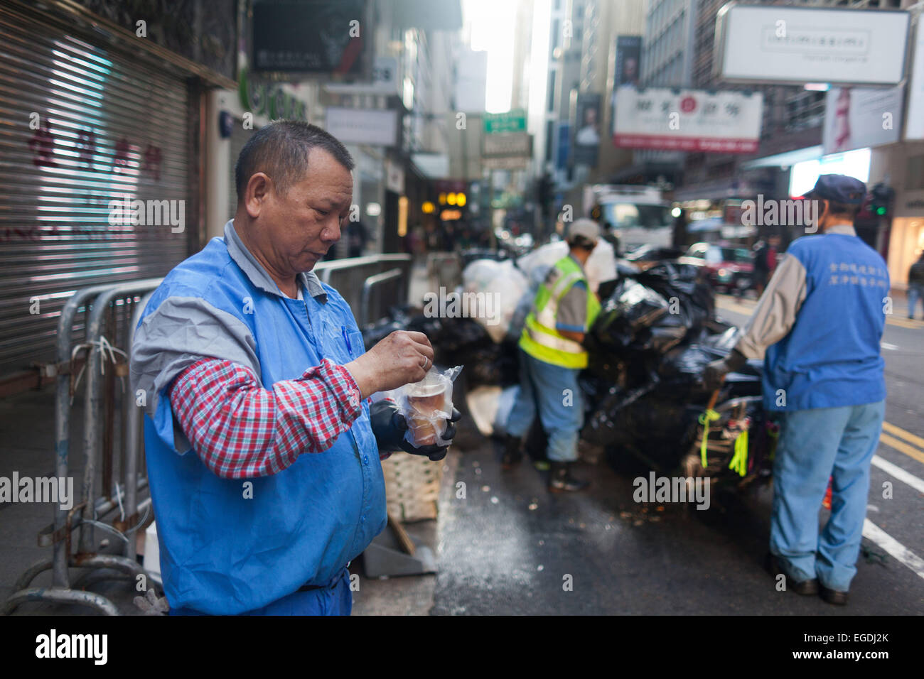 Straßenreinigung bei der Arbeit im Central Business District von Hong Kong. Der Manager macht eine kurze Pause und trinken hat. Stockfoto