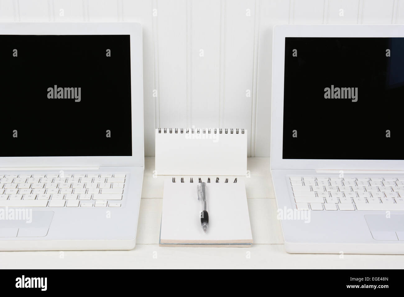 Nahaufnahme von zwei Laptops in einem weißen Arbeitsplatz mit Pad und Stift in der Mitte. Die Computer sind gegen eine Beadboard Wand mit b Stockfoto