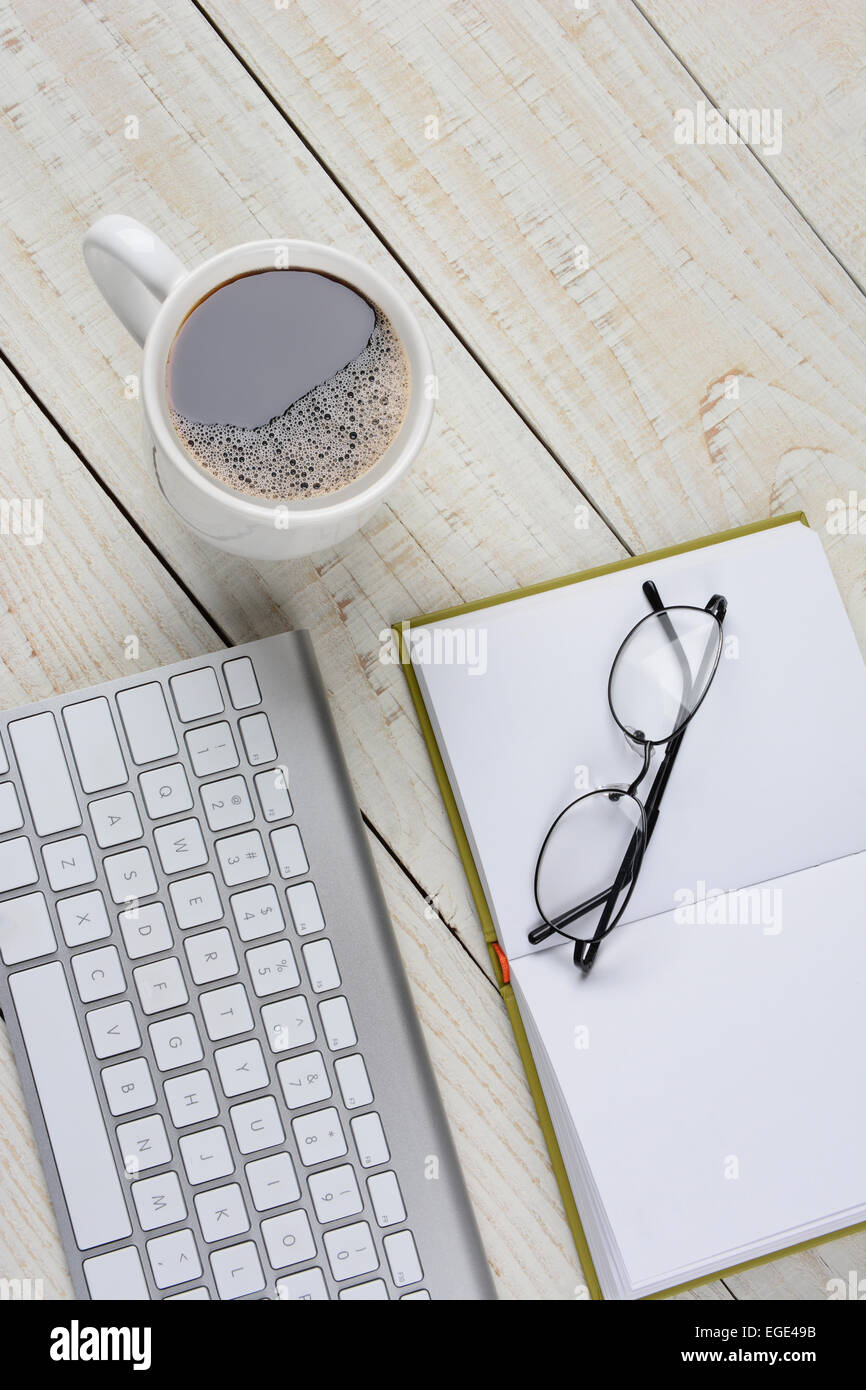 Vertikale Overhead Schuss von einem home-Office Schreibtisch mit einer Tasse Kaffee und Buch mit Brille und eine Computer-Tastatur zu öffnen. Das Element Stockfoto