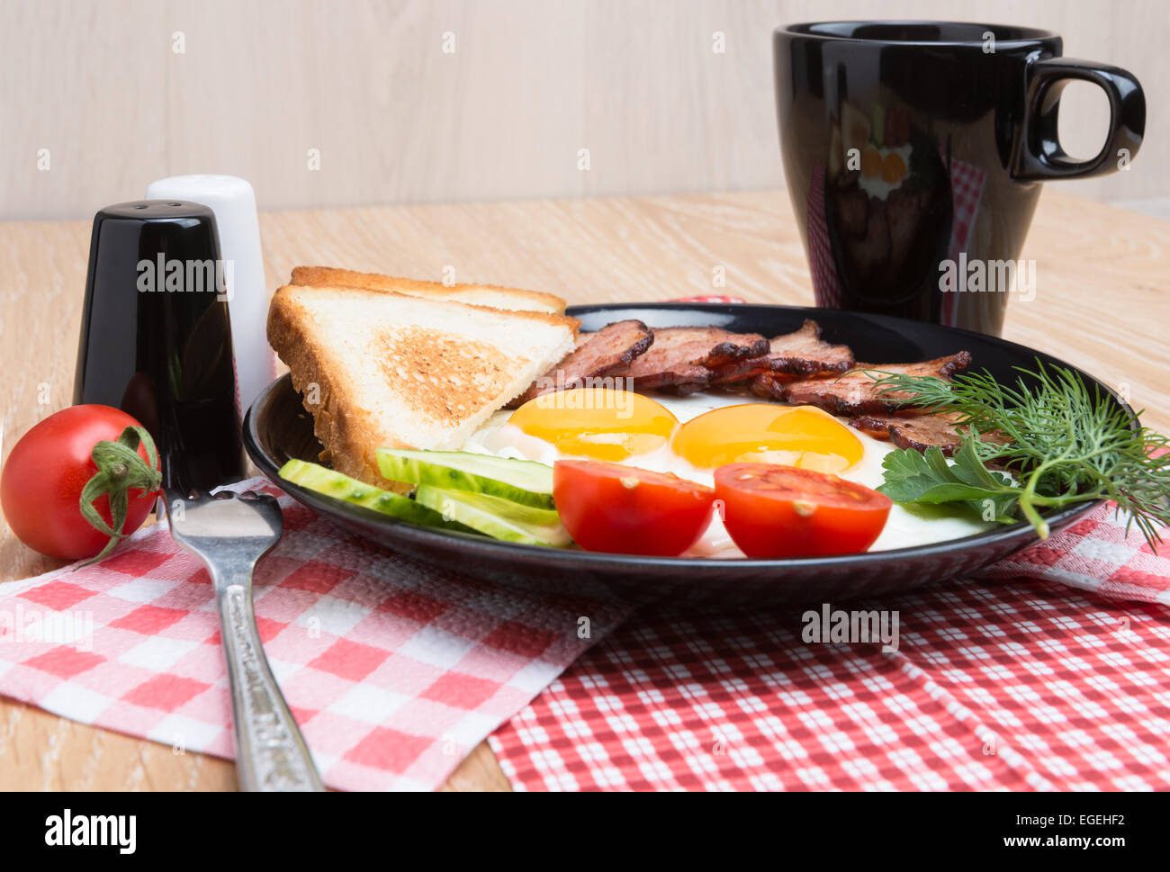 Spiegeleier mit Speck, Brot, Kaffee und Gemüse auf schwarzem Teller Stockfoto