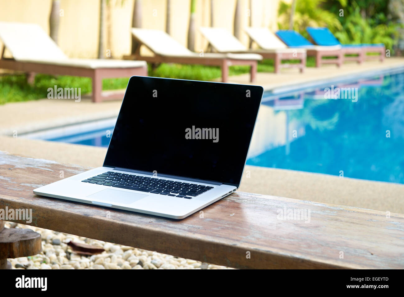 Laptop auf einer Bank am Pool, im Urlaub mit Mobilitätskonzept arbeiten Stockfoto