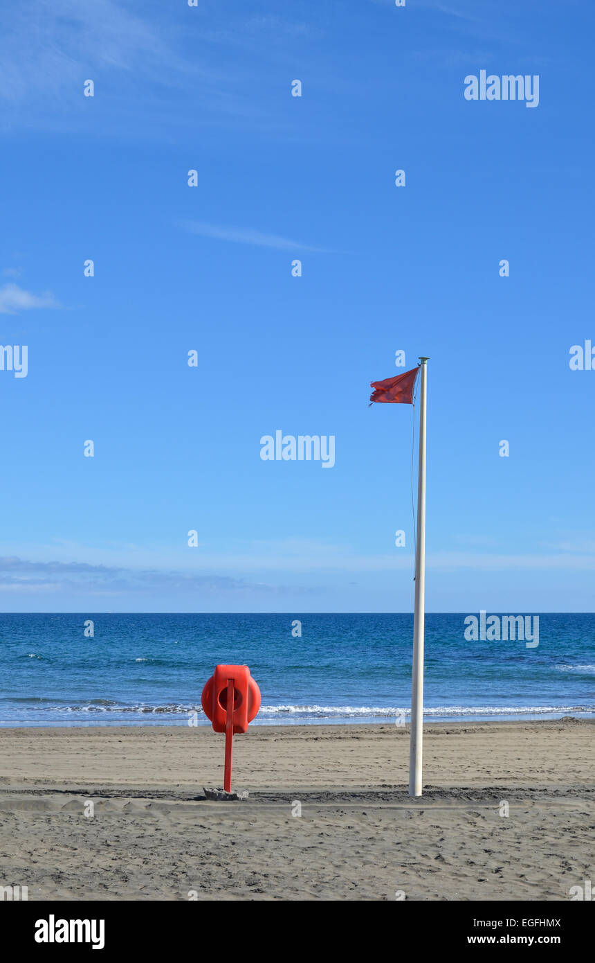 Rote Warnung Flagge und einen Rettungsring an einem sonnigen Strand mit klaren, blauen Himmel Stockfoto