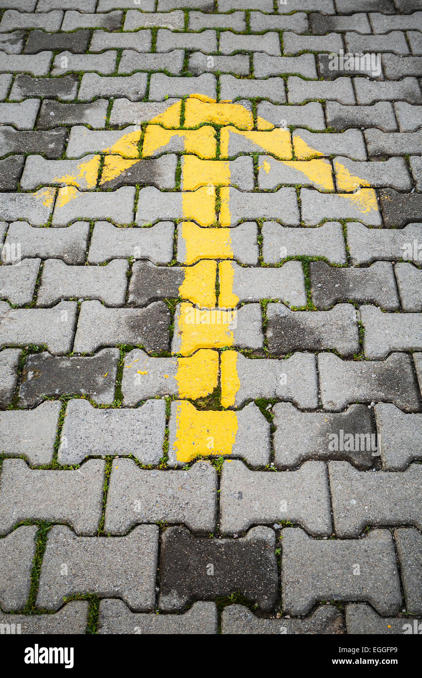 Gelber Pfeil auf graue Kopfsteinpflaster, Richtung Straßenschild Stockfoto