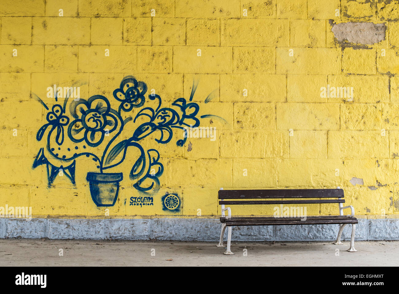 Blaue Graffiti Blumen auf gelb lackierten Steinmauer mit einer Bank an der Wand Stockfoto