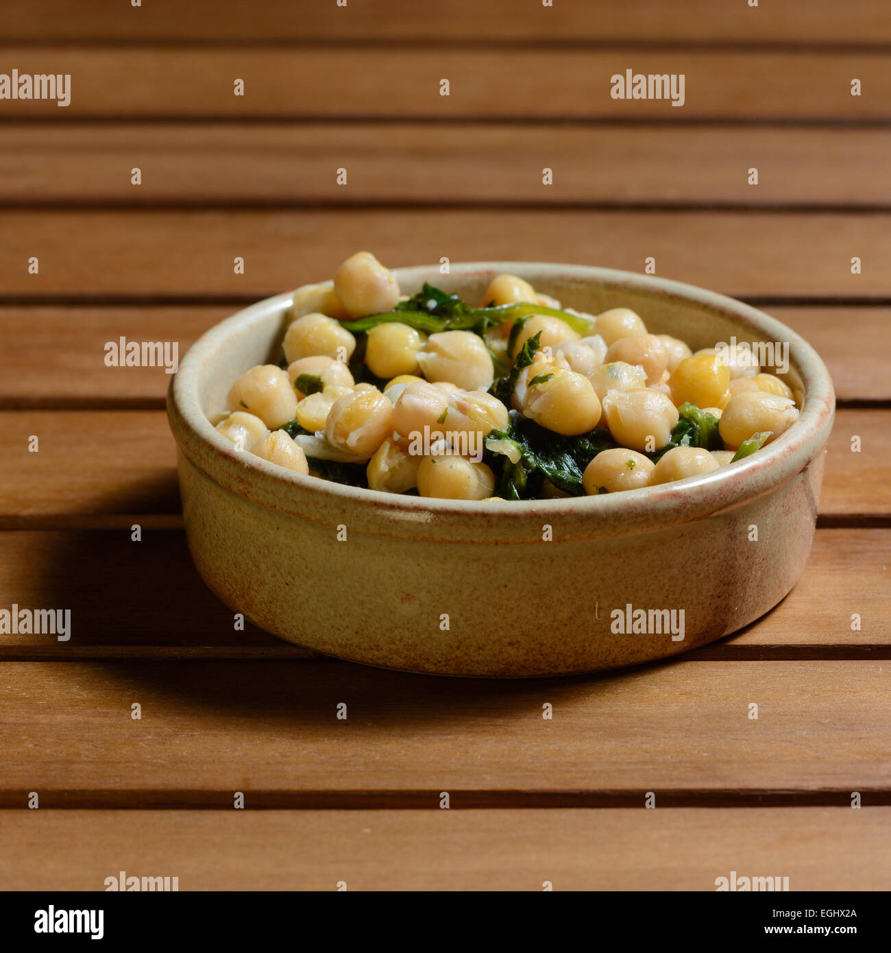 Tapas. Kichererbsen & Spinat gekocht eine würzige vorrätig, serviert in einer braunen Keramikschüssel auf einer hölzernen Tischplatte Stockfoto