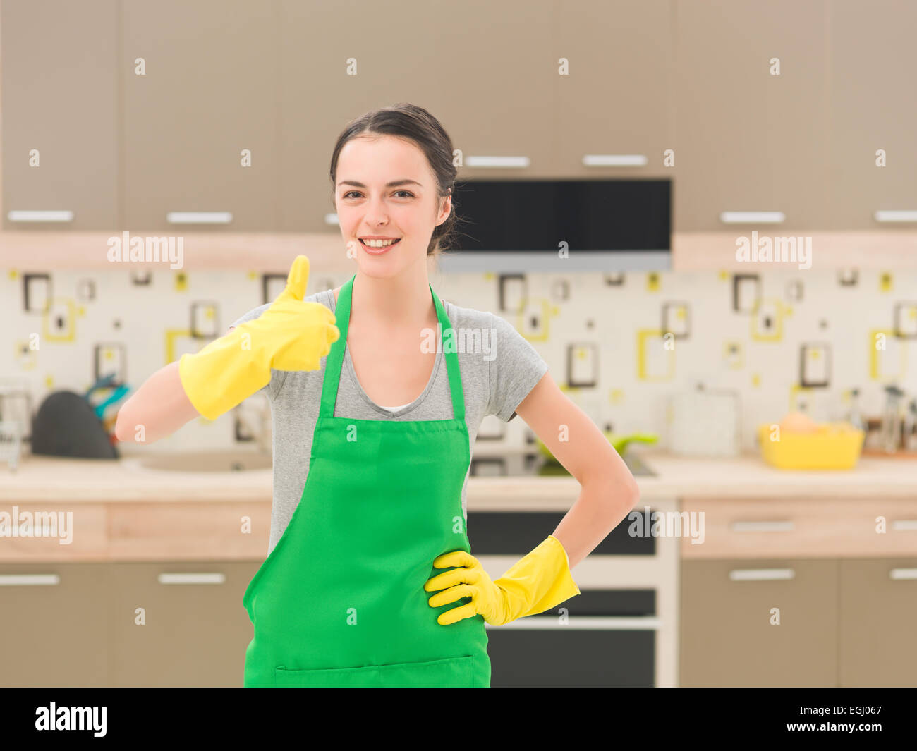 Putzfrau glücklich und aufgeregt, stehend in Küche, Daumen auftauchen Stockfoto