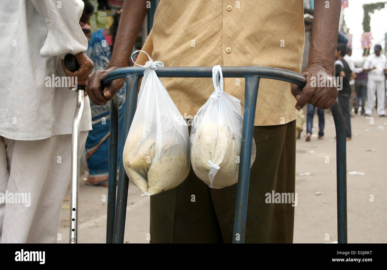 Alten behinderten Mann tragen Nahrung gebunden, die Krücke in einer belebten Straße am Juli 28,2013 in Hyderabad, AP, Indien. Stockfoto