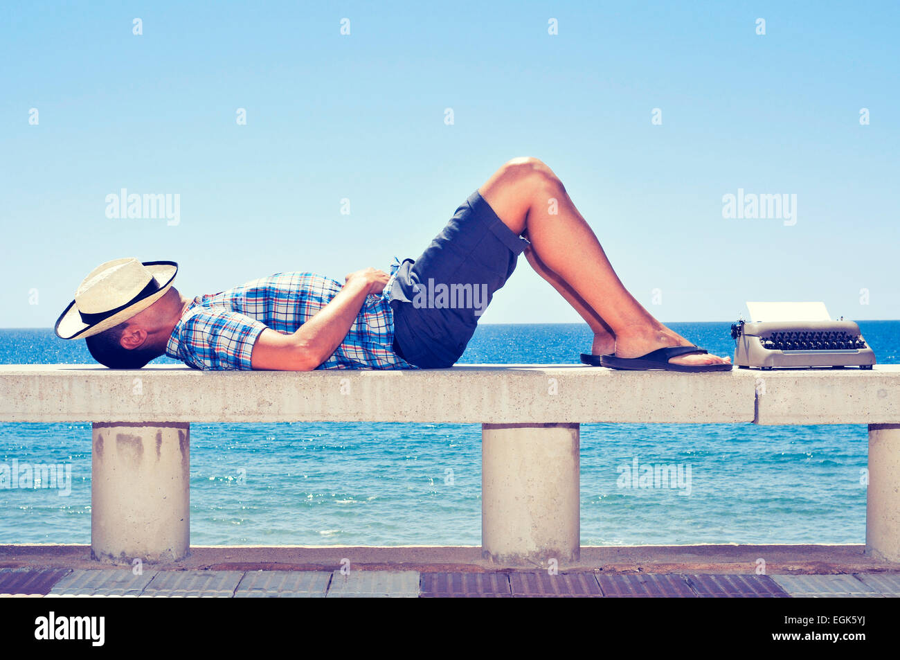 einer alten Schreibmaschine Weile wartet mit einer leeren Seite und ein junger Mann in einer Straße Bank am Meer liegend, Inspiration Stockfoto