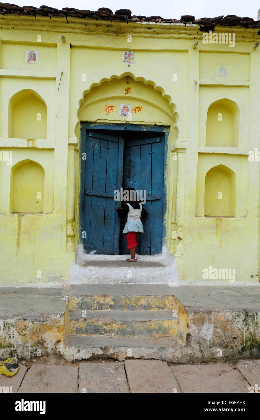 Kleine Inderin, die zu Fuß in ein gelb und blau bemalte Haus Orchha Madhya Pradesh, Indien Stockfoto