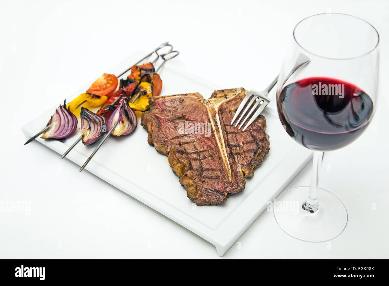T-bone Steak auf einem weißen Teller mit gegrilltem Gemüse und ein Glas Rot Wein Schuss auf weiß Stockfoto