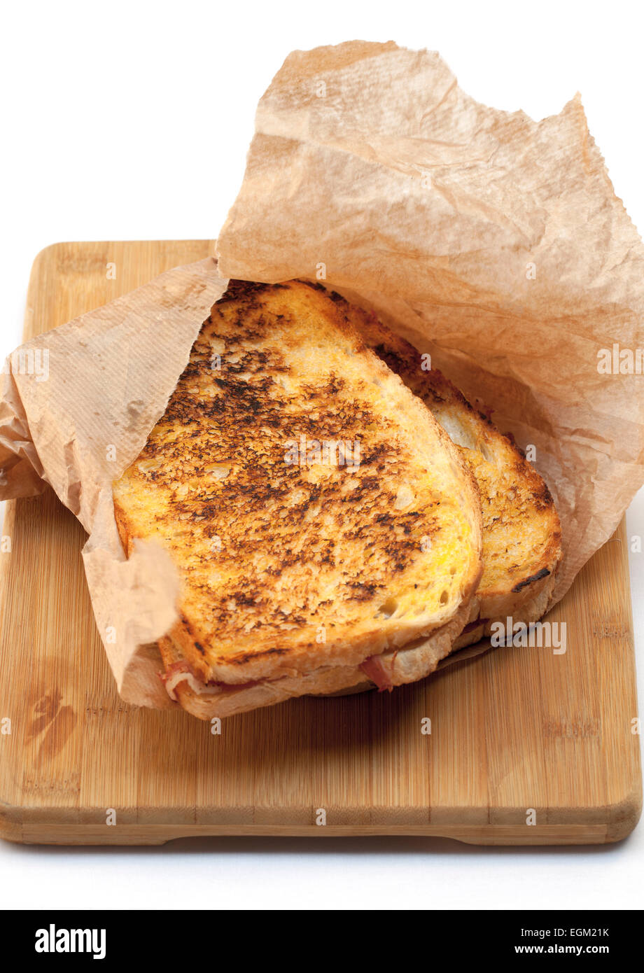 Geröstete Gourmet-Schinken und Käse-Sandwich in braune Papiertüte auf hölzernen Brot-Brett Stockfoto