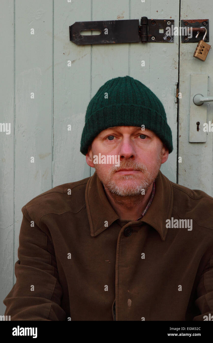 Portrait Mann mittleren Alters im Alter von 50 Jahren tragen Arbeitskleidung und Wolly Hut außerhalb ein Schuppen Garagentor UK Stockfoto