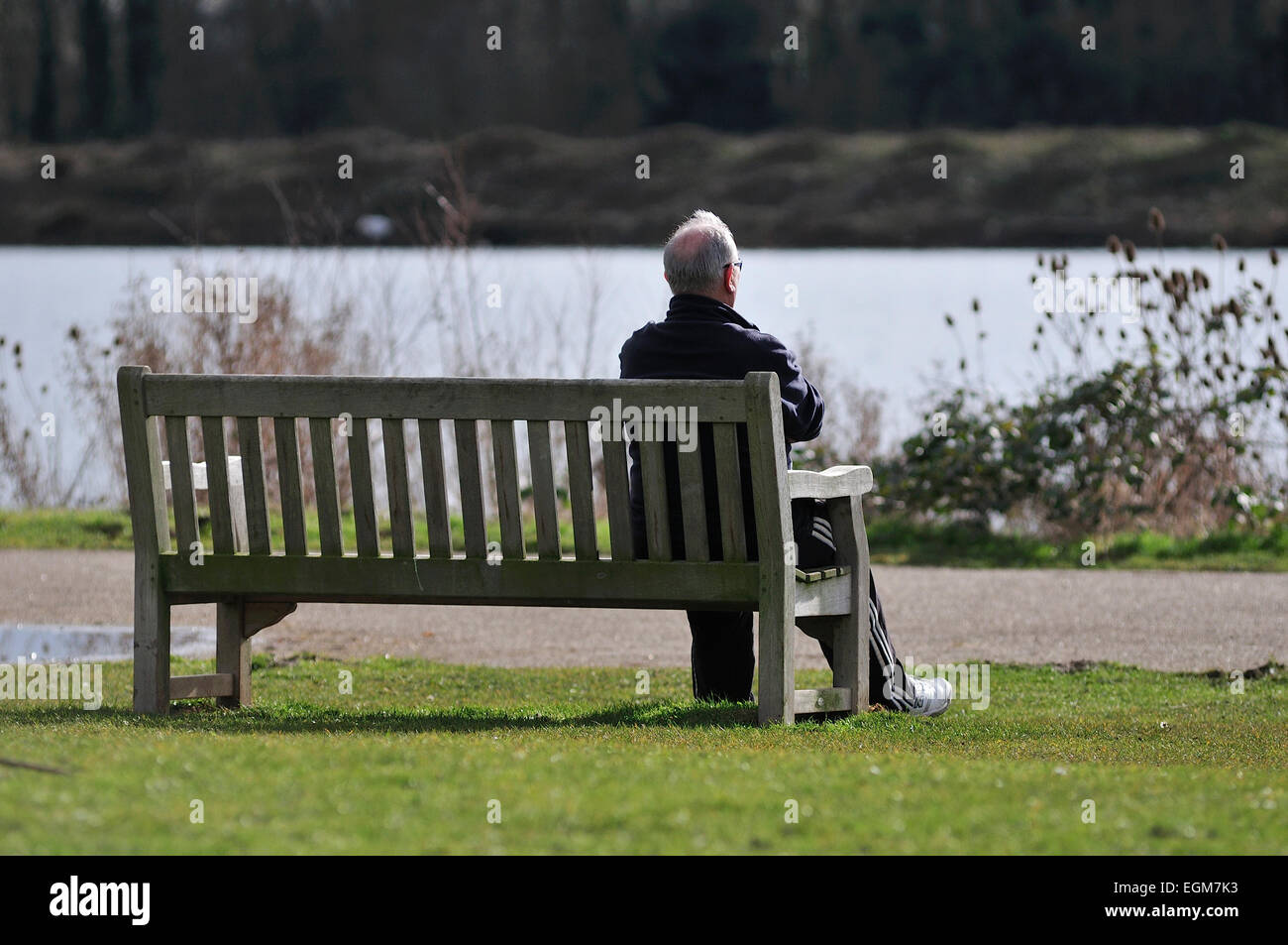 Älterer Mann sitzt allein auf einer Parkbank Stockfoto