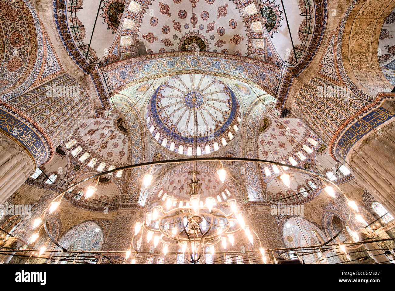 Sultan-Ahmed-Moschee Kuppeln und Kronleuchter Istanbul // ISTANBUL, Türkei — die reich verzierten Kuppeln und Halbkuppeln der Sultan-Ahmed-Moschee zeigen komplizierte islamische Kalligraphie und geometrische Muster. Traditionelle osmanische Kronleuchter (Kändil), die an den Kuppeln hängen, beleuchten die berühmten blauen Iznik-Fliesen der Moschee. Die komplexe architektonische Anordnung der kaskadierenden Kuppeln stellt den Höhepunkt der klassischen osmanischen Moschee dar. Stockfoto