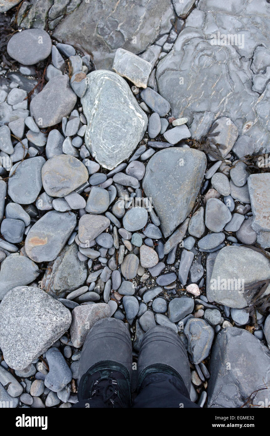 Die Füße der Wanderer im Winter Stiefel stehen auf einer steinigen Küste. Stockfoto