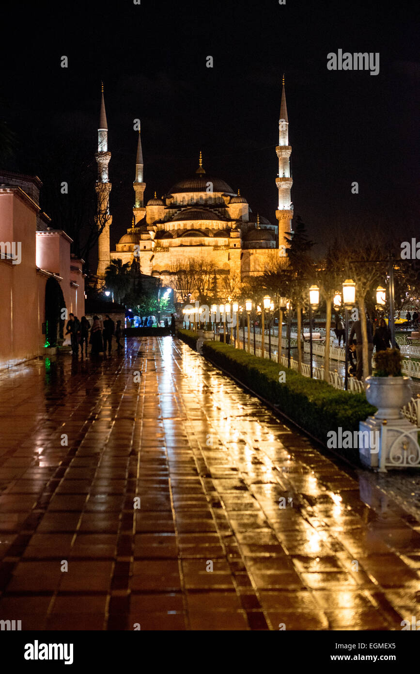 ISTANBUL, Türkei – die beleuchtete Sultan-Ahmed-Moschee spiegelt sich in regengeschliffenen Pflastersteinen des Sultanahmet-Platzes bei Nacht. Die kaskadierenden Kuppeln und sechs Minarette der Moschee bilden eine dramatische Silhouette vor dem Abendhimmel. Der nasse Bürgersteig spiegelt die architektonischen Elemente der Moschee wider und verdoppelt die visuelle Wirkung der nächtlichen Beleuchtung. Stockfoto