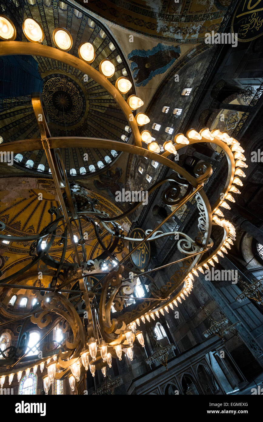 ISTANBUL, Türkei – Ein traditioneller osmanischer Kronleuchter beleuchtet das riesige Innere der Hagia Sophia. Dieser runde, mehrstufige Kronleuchter, auch bekannt als „Avize“, wurde für zahlreiche Öllampen entworfen. Das massive Gebäude aus dem 6. Jahrhundert, das im Laufe seiner Geschichte sowohl als Kirche als auch als Moschee diente, verfügt über mehrere dieser osmanischen Leuchten, die an der hoch aufragenden Kuppel hängen. Stockfoto