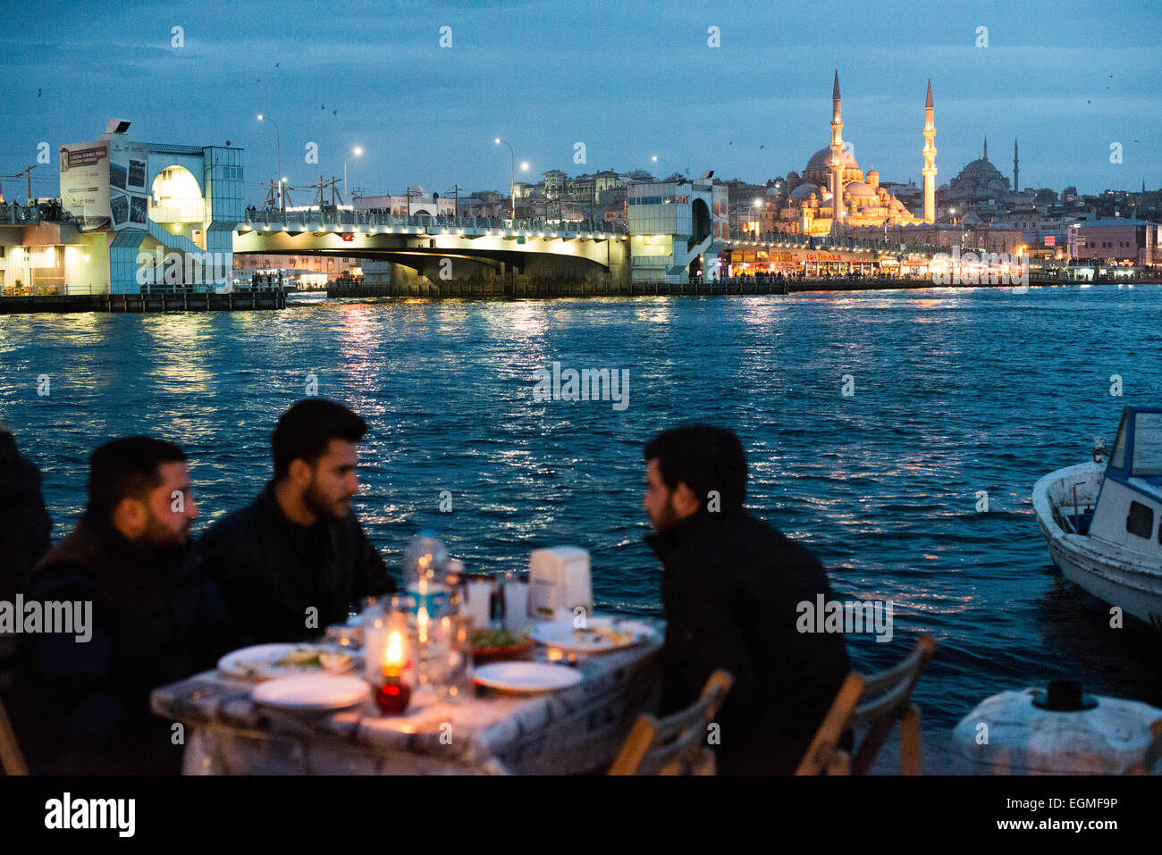 Golden Horn Waterfront Restaurants Istanbul // ISTANBUL, Türkei – die Gäste genießen ihre Mahlzeiten in Restaurants im Freien am Golden Horn Waterfront in Karakoy, Istanbul. Die historische neue Moschee (Yeni Cami), die 1665 fertiggestellt wurde, und die Galata-Brücke bilden eine dramatische Kulisse. Diese beliebten Restaurants am Wasser bieten frische Meeresfrüchte und traditionelle türkische Küche mit Blick auf die historische Skyline Istanbuls. Stockfoto