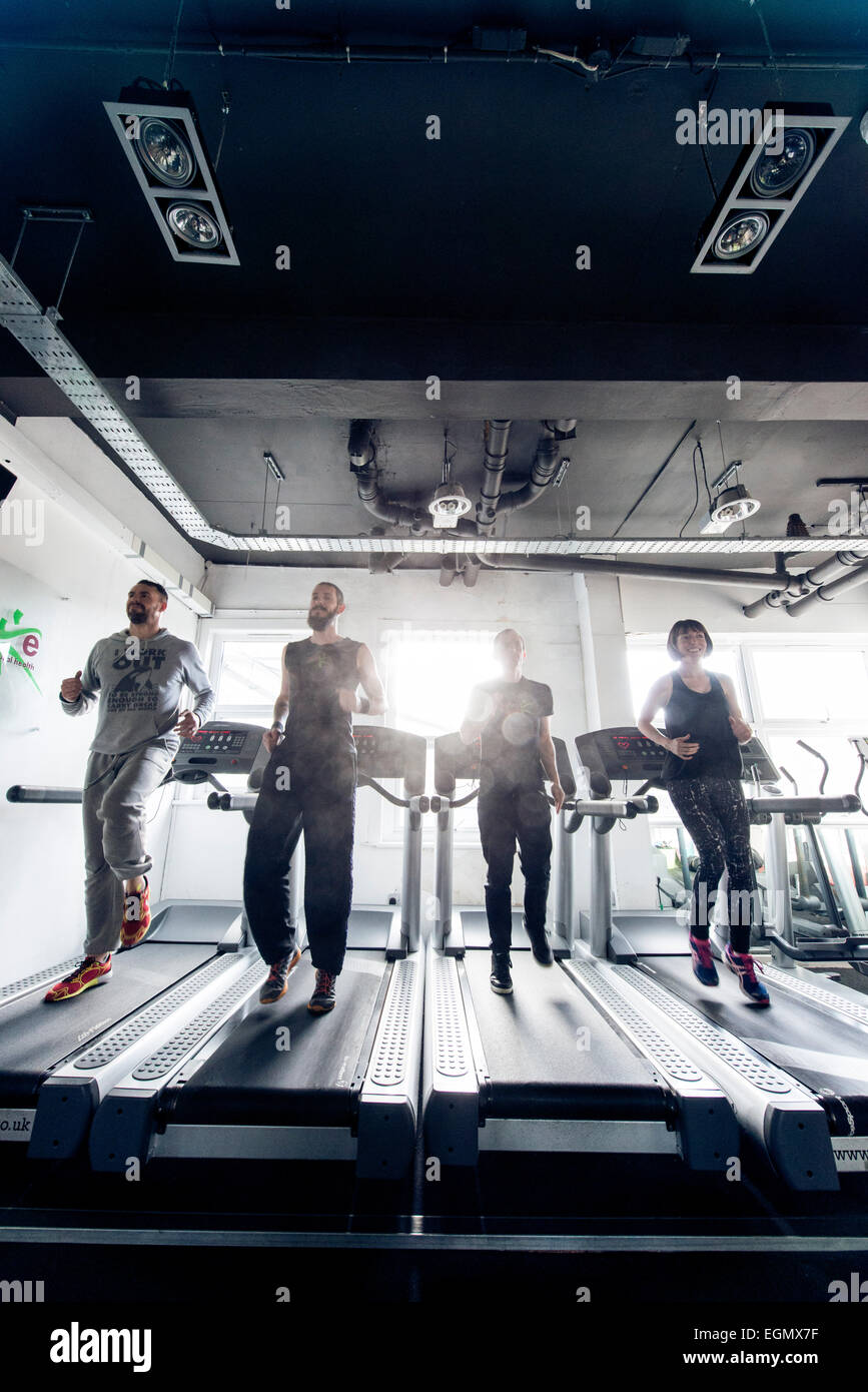 Weitwinkel-Aufnahme von vier Fitness-Profis / Trainer, Joggen am laufenden Maschinen / Laufbänder in einer Turnhalle im Laufe des Tages Stockfoto
