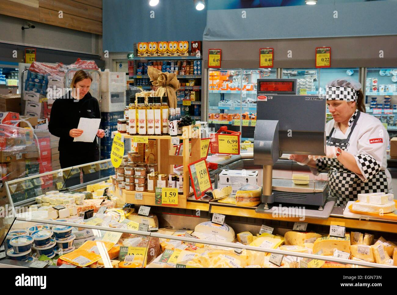 Riga Lettland. Innere des Rimi Hypermarkt lettischen Shop. Assistent und Kunden an Milchprodukten Deli Käsetheke mit Einkaufsliste Stockfoto