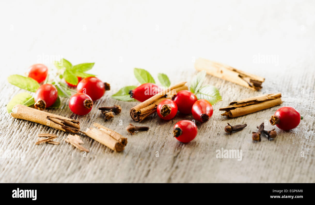 Hagebutte, Rosa Canina. Einige Hüften angeordnet mit Blättern und Stücke von Zimtstange und Nelken auf blass, distressed, hölzernen Hintergrund. Selektiven Fokus. Stockfoto