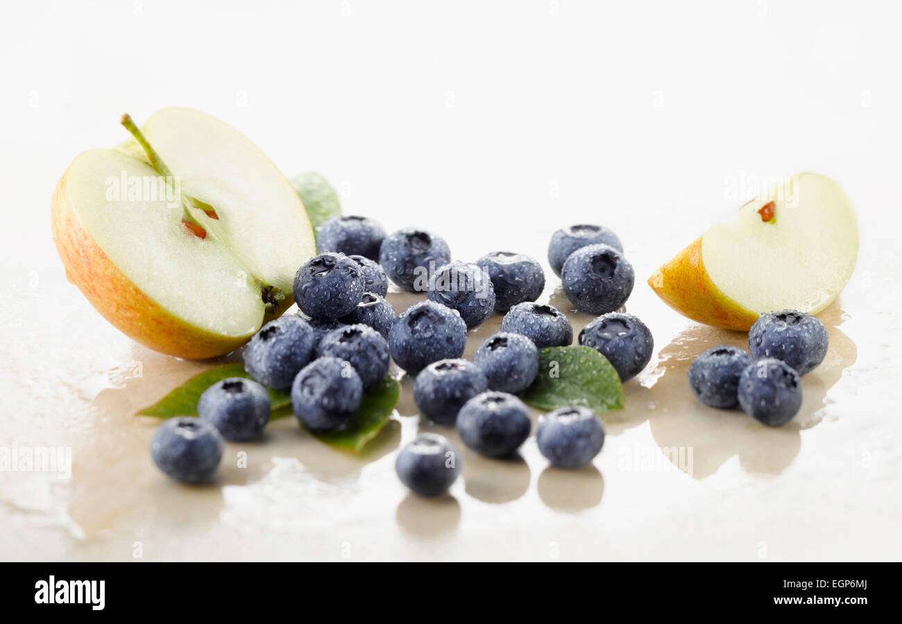 Heidelbeere, Vaccinium Corymbosum Sorte. Mehrere Beeren mit einer halben und Viertel von Apple und spritzed mit Wasser auf weißem Marmor angeordnet. Selektiven Fokus. Stockfoto