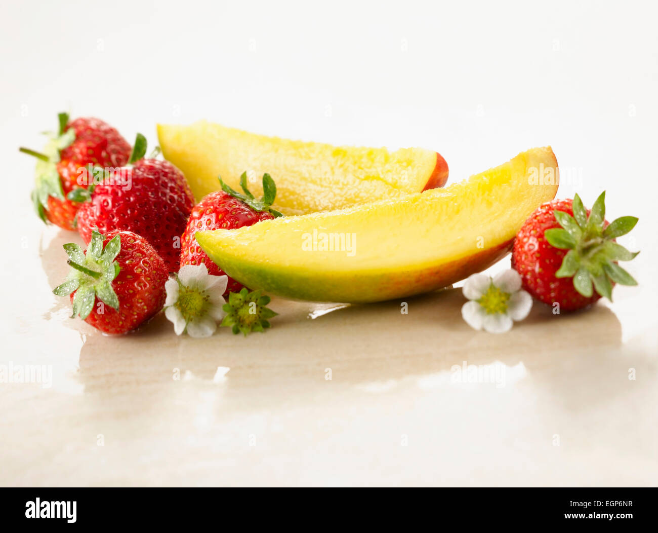 Mango, Mangifera Indica. Zwei Scheiben angeordnet mit Erdbeeren, Fragaria Sorte und Blumen auf weißem Marmor. Selektiven Fokus. Stockfoto